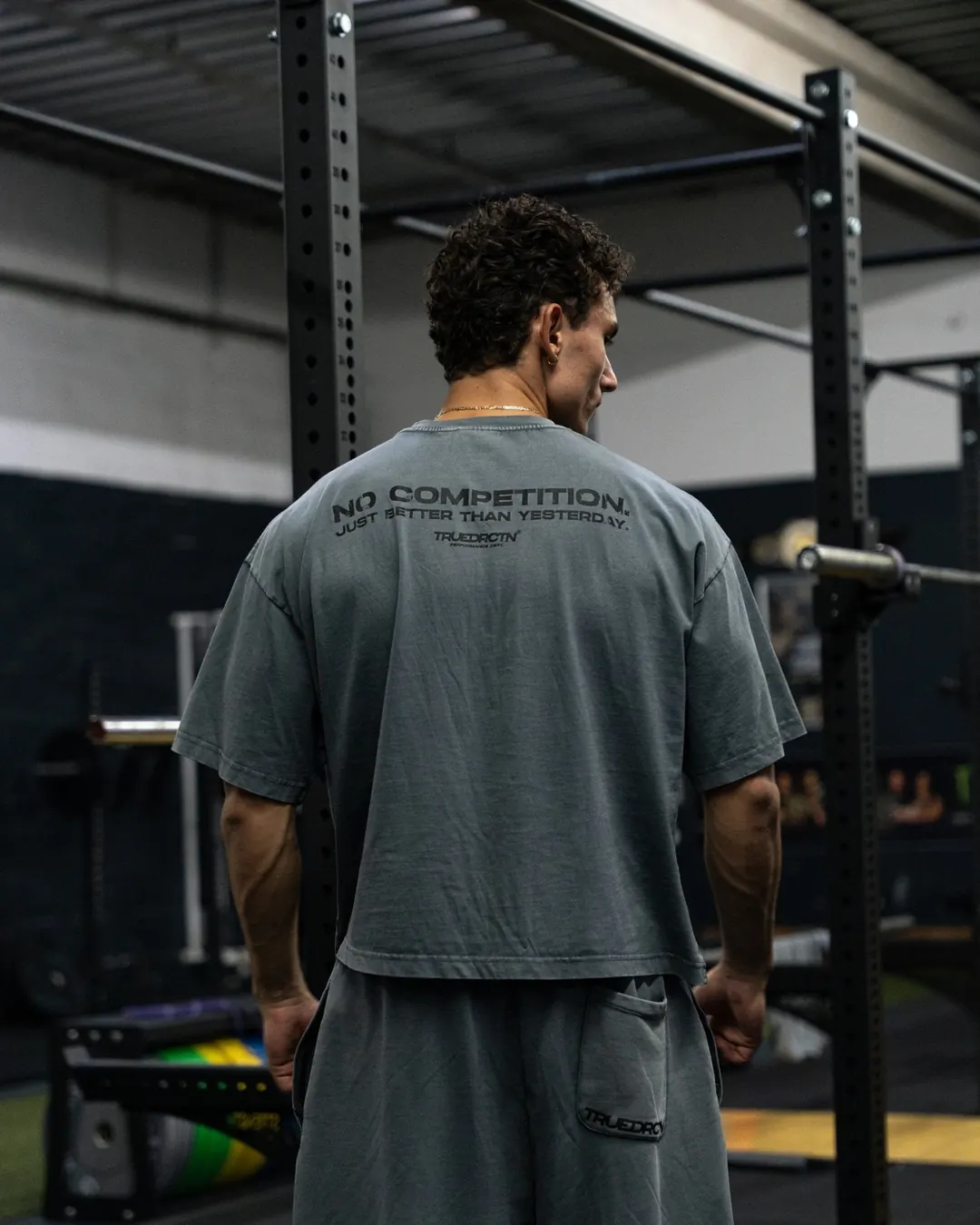 Athlet von hinten im grauen No Competition Tee zwischen Racks